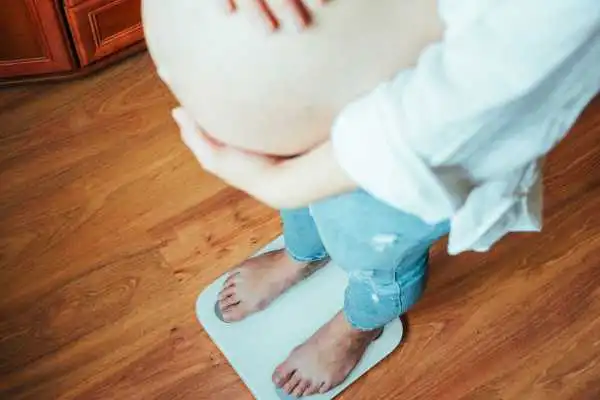 Image of woman weighing herself and experiencing weight gain through pregnancy Merthyr Tydfil